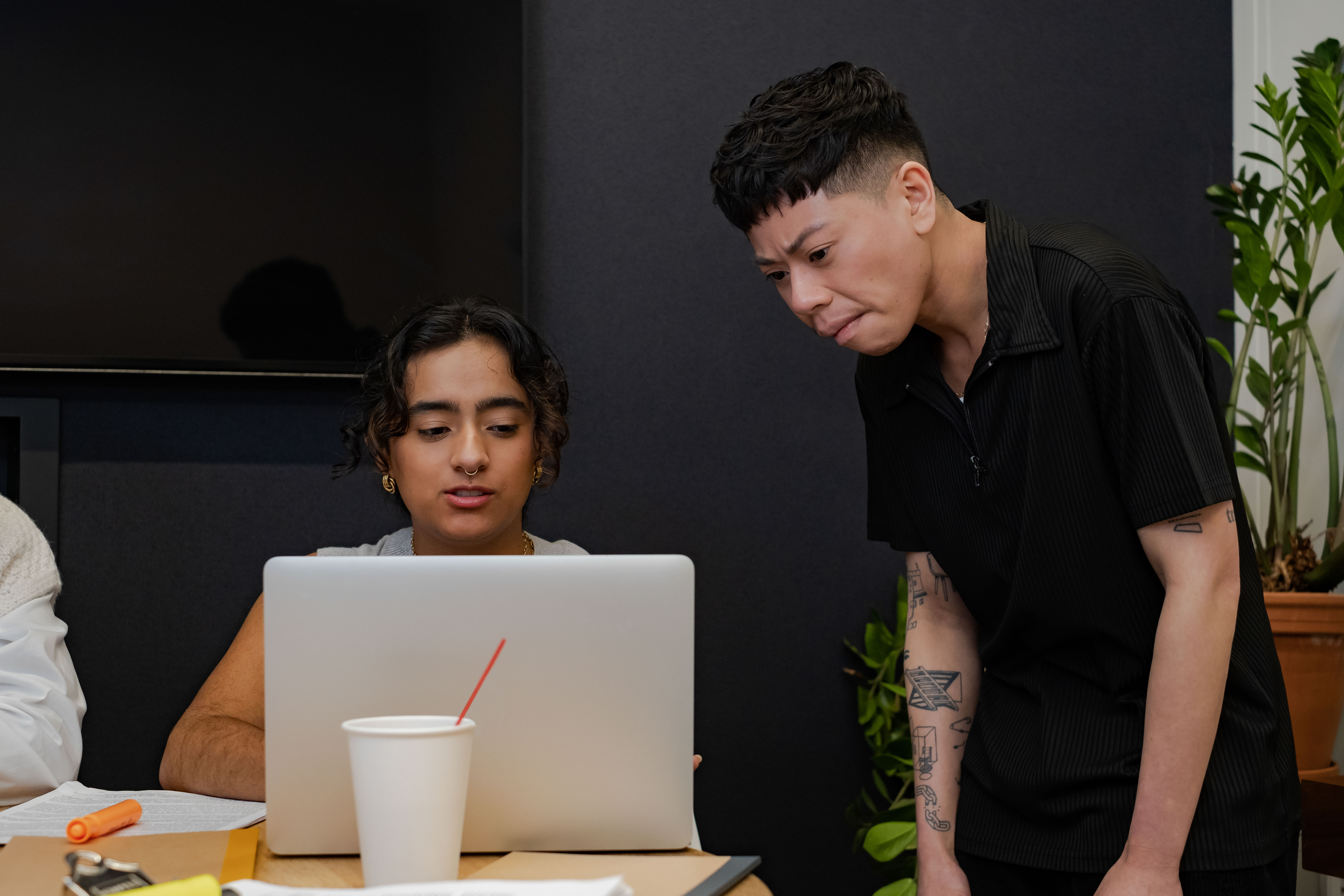 A trans man showing a non-binary colleague something on a laptop